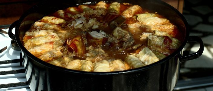 A black cast-iron pot of Romanian sarmale, cabbage rolls stuffed with minced pork and rice, simmering in their sauce on a stovetop.