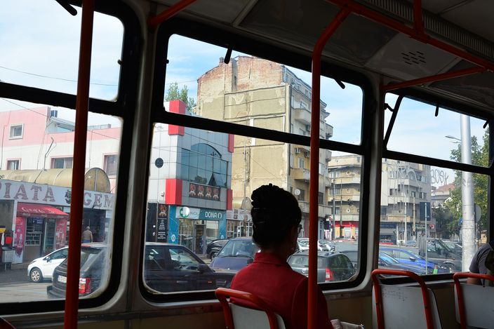 View from inside a Bucharest tram through the windows: a passenger in a red seat looks out at Piața Gemeni, with shopfronts, parked cars and traffic along Strada Vasile Lascăr.