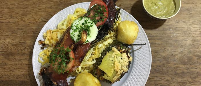 A whole roasted guinea pig (cuy al horno) splayed on a white plate with boiled potatoes and a green huacatay sauce, served in Cusco