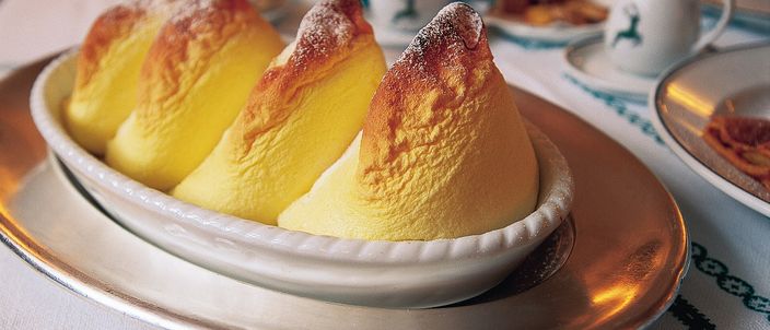 A Salzburger Nockerl served in a white oval dish: three tall golden-baked peaks dusted with icing sugar, on a laid restaurant table.