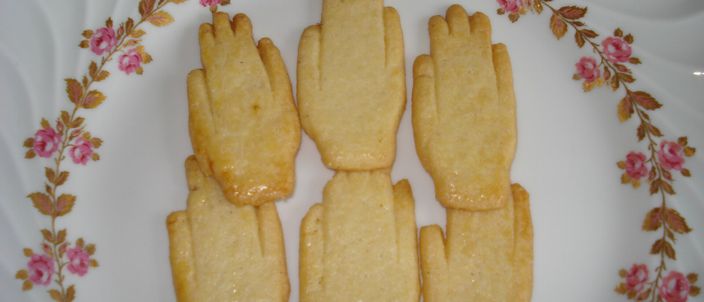 Three hand-shaped Antwerpse handjes biscuits, glazed pale gold, arranged on a floral-rimmed plate