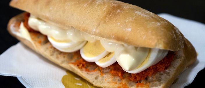 A crusty roll filled with pink filet américain and sliced hard-boiled egg, on a paper napkin