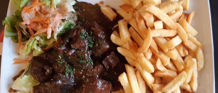 A plate of stoverij: dark beer-braised beef chunks in glossy sauce beside a generous pile of frites, with a small salad garnish
