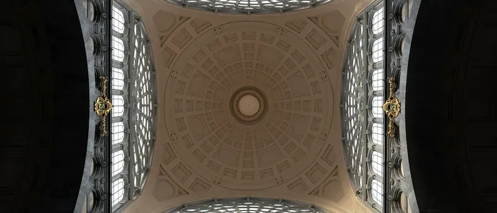 Looking straight up into the coffered stone-and-plaster dome over the main hall of Antwerpen-Centraal station, a circular oculus at its center and tall arched windows filling the four sides.
