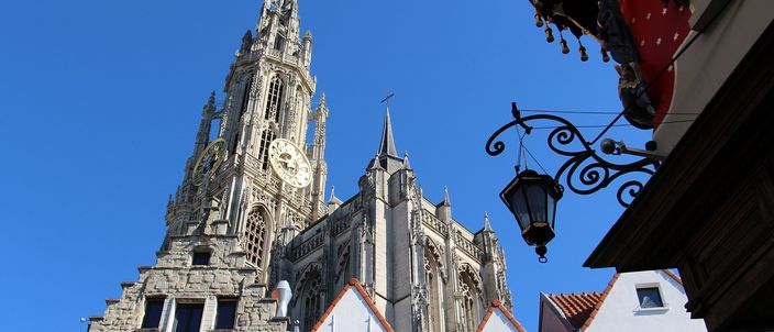 The cathedral of Our Lady's single completed north tower rising over the gabled houses at its foot, seen from the square below against a deep blue sky.