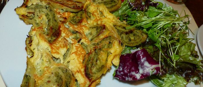 Pan-fried slices of Maultaschen set in golden egg, their green-flecked spiral filling showing, with a side salad on the plate.