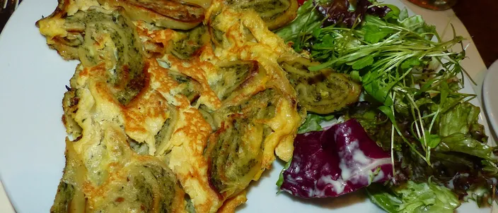 Pan-fried slices of Maultaschen set in golden egg, their green-flecked spiral filling showing, with a side salad on the plate.
