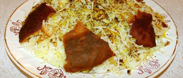 A plate of Azerbaijani plov: a mound of saffron-streaked rice with large pieces of golden-brown qazmaq crust broken over the top, on a patterned white plate.
