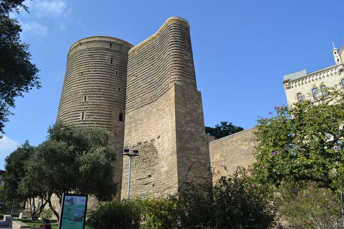 Maiden Tower, Icherisheher: a round eight-storey stone tower beside the old city wall, blue sky behind it