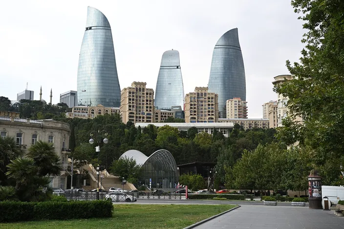 The three glass-clad Flame Towers rising above Baku's hillside greenery, seen from the waterfront promenade under a clear blue sky.