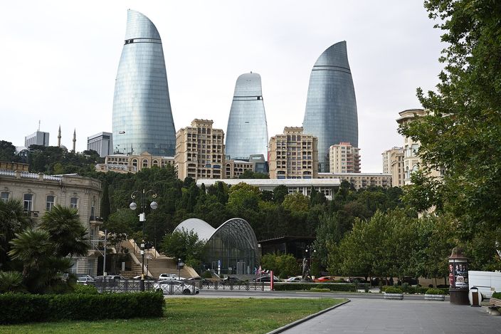 The three glass-clad Flame Towers rising above Baku's hillside greenery, seen from the waterfront promenade under a clear blue sky.