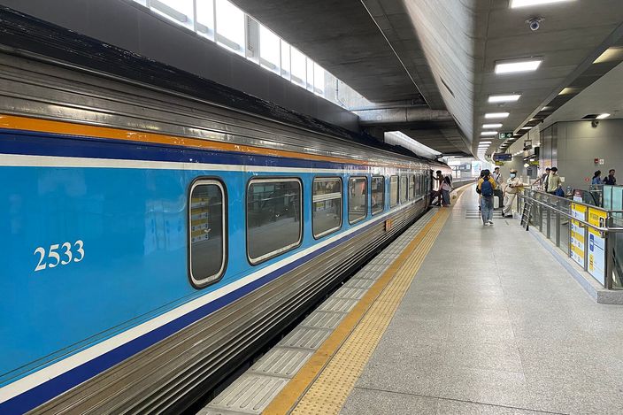 A blue-and-white State Railway of Thailand carriage numbered 2533 standing at a platform inside Krung Thep Aphiwat Central Terminal, passengers waiting beside the open doors under a concrete ceiling and strip lighting.