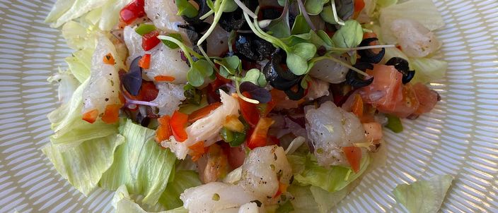 A plate of esqueixada de bacallà: pale, hand-torn flakes of salt cod with black olives, chopped red pepper and cress, on a bed of lettuce.