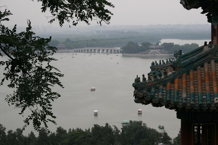 Kunming Lake seen from the temple terrace on Longevity Hill, framed by a painted eave in the foreground, with the long arched bridge crossing the water below
