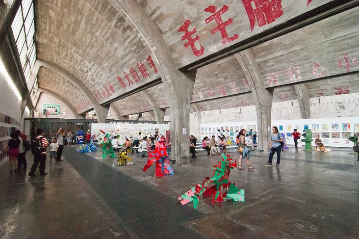 Inside a sawtooth-roofed hall of the 798 Art Zone, the original factory slogans still painted across the concrete vaults above people using the space