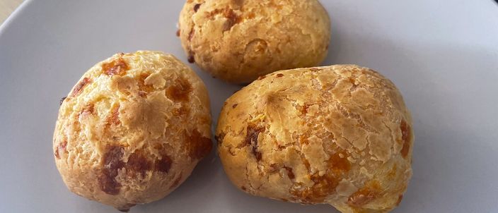 Three golden-baked pão de queijo cheese rolls on a white plate, their crusts flecked with browned cheese.