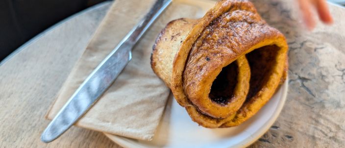 A cinnamon bun on a plate, its spiral of cinnamon dough visible from the top.