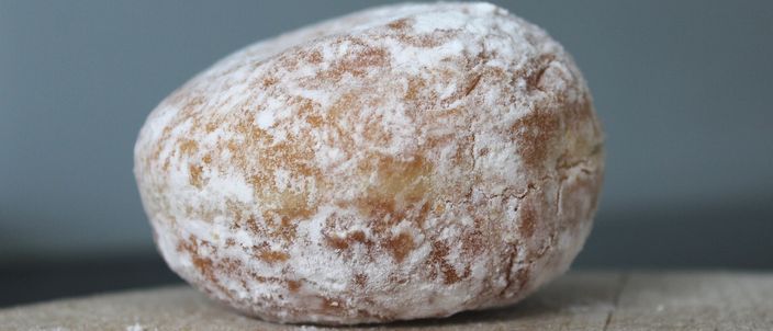 A single sugar-dusted Berliner doughnut on a wooden board, the pale band around its middle visible