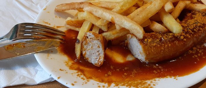 A currywurst sliced into pieces under a red curry-tomato sauce, dusted with curry powder, a heap of chips beside it.