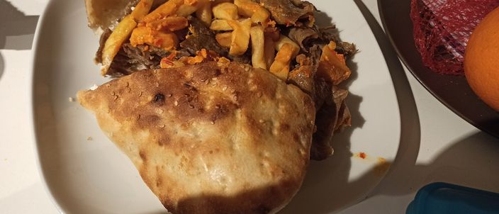 A German-style doner: carved meat and salad stuffed into a folded flatbread, served on a plate with a side of chips and chilli sauce.