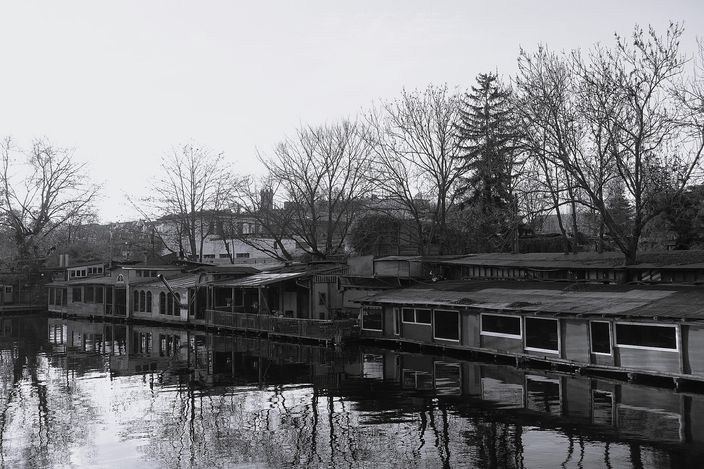 Old houseboats moored along the Flutgraben canal in Berlin-Kreuzberg, bare winter trees reflected in still dark water