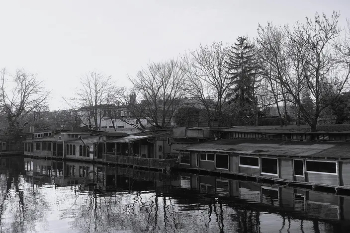 Old houseboats moored along the Flutgraben canal in Berlin-Kreuzberg, bare winter trees reflected in still dark water