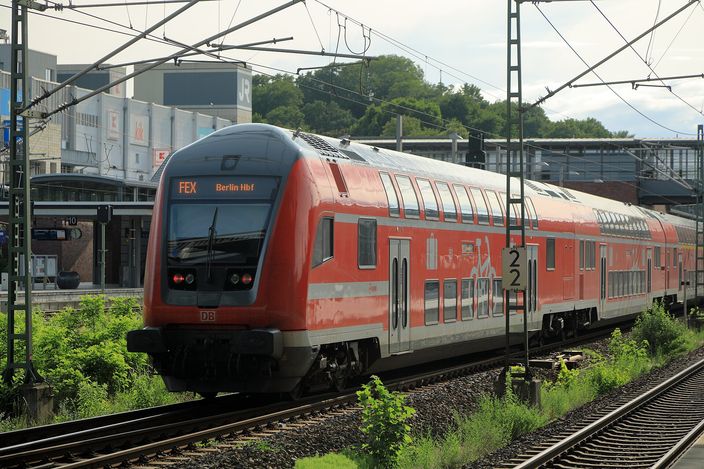 A red Deutsche Bahn double-decker regional train with 'FEX Berlin Hbf' on its front destination display, running along tracks under overhead wires at Berlin Gesundbrunnen station.