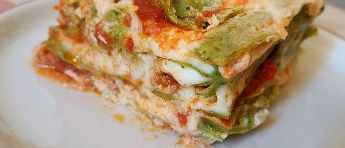 A cross-section slice of green-pasta lasagne on a plate, showing layers of spinach sheets, pale béchamel and meat ragù