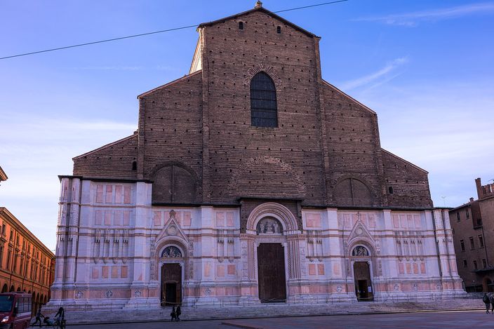 The unfinished facade of the Basilica di San Petronio in morning light on Bologna's Piazza Maggiore: a lower band of white and pink marble below bare brick.