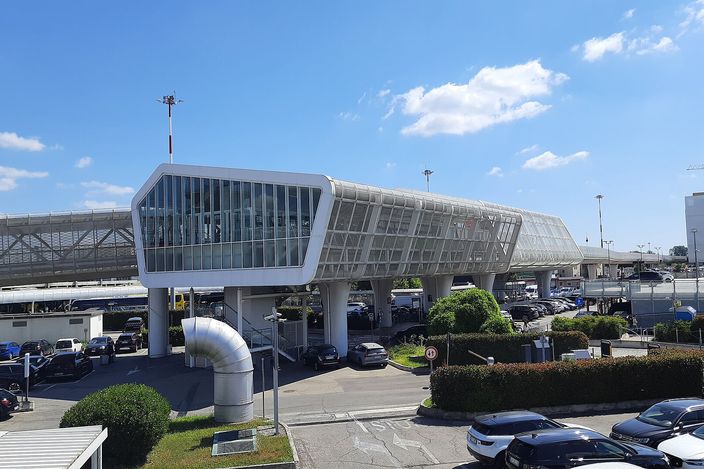 The Marconi Express monorail: a glazed elevated guideway curving away from its station on white concrete piers, under a clear sky at Bologna airport.