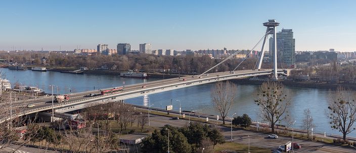 The Most SNP cable-stayed bridge crossing the Danube in clear winter light, its single angled pylon topped by a flying-saucer-shaped restaurant deck, with the tower blocks of Petrzalka lining the far bank behind it.