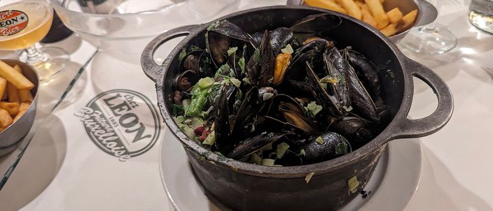 A black cast-iron pot of steamed mussels with a separate portion of chips on a restaurant table in Belgium