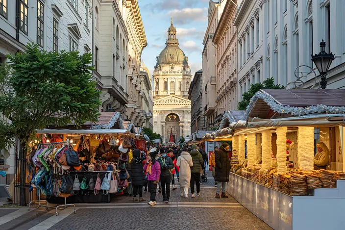 Market stalls lining a street of grand apartment fronts in Budapest's inner city, a chimney-cake stall in the foreground and the dome and front of St Stephen's Basilica closing the view