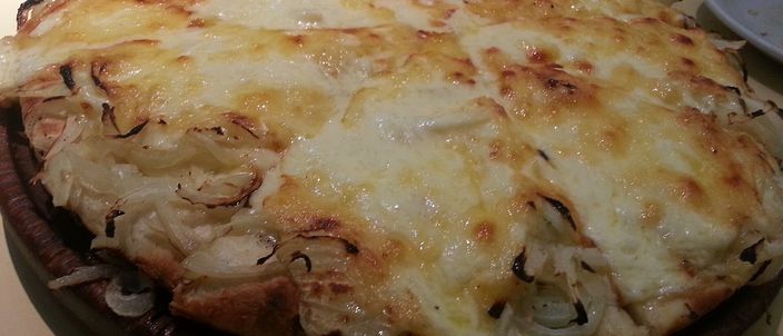 A whole round Argentine fugazza con queso on a plate, its surface a golden layer of melted cheese scattered with softened onion
