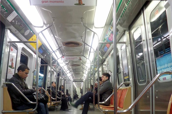 Interior of a Buenos Aires Subte metro carriage with passengers seated along both sides, stainless-steel poles and overhead Spanish-language advertising