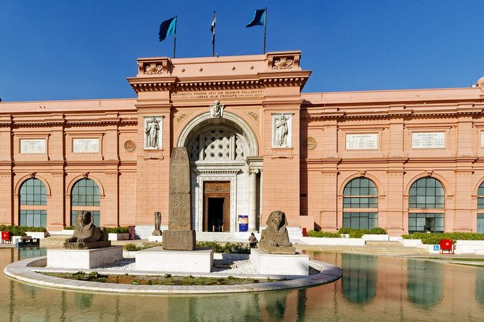 The pink neoclassical facade of the Egyptian Museum on Tahrir Square, its reflecting pool and flanking sphinx statues in front of the entrance under a clear sky.