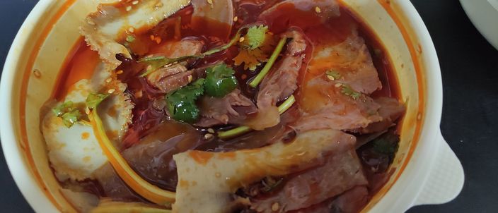 A bowl of fuqi feipian: thin slices of beef and offal fanned in a deep red chilli-oil dressing, topped with fresh coriander and slivered aromatics.