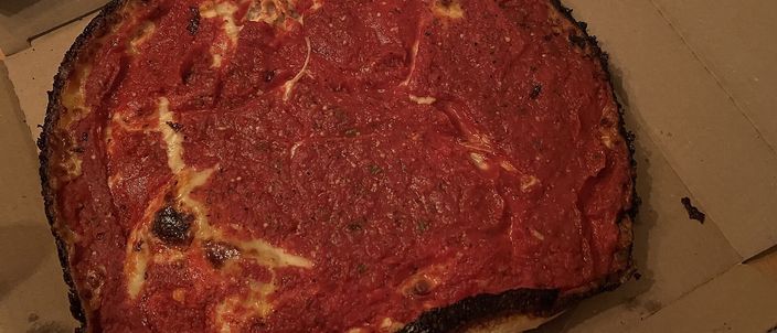 A deep pan pizza with a dark caramelised crust rim and a top layer of chunky red tomato sauce over the cheese, in an open box.