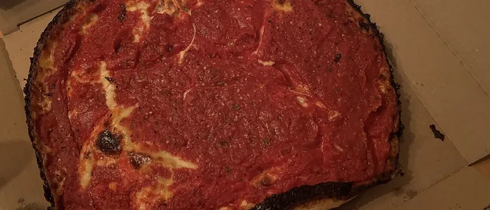 A deep pan pizza with a dark caramelized crust rim and a top layer of chunky red tomato sauce over the cheese, in an open box.
