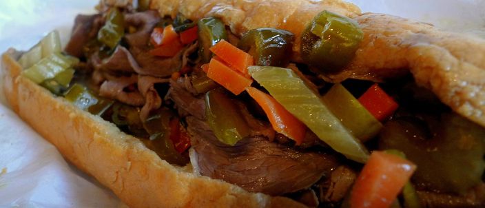 A Chicago Italian beef sandwich on a long roll, piled with thin-sliced beef and heaped with colourful hot giardiniera of pickled peppers, celery and carrot.