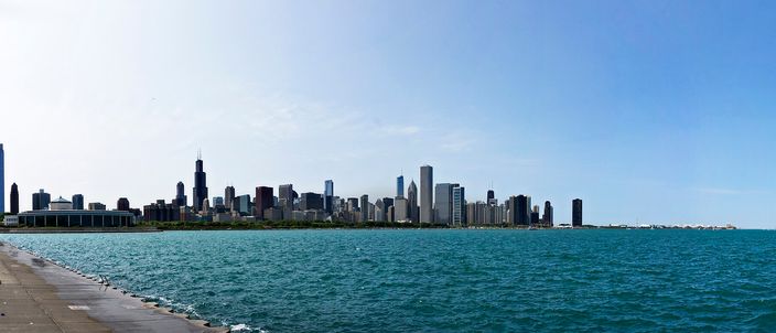 Chicago's downtown skyline seen across Lake Michigan from the Museum Campus, the Sears/Willis Tower at left and a wide sweep of towers meeting the blue water and lakefront path in the foreground