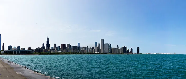 Chicago's downtown skyline seen across Lake Michigan from the Museum Campus, the Sears/Willis Tower at left and a wide sweep of towers meeting the blue water and lakefront path in the foreground