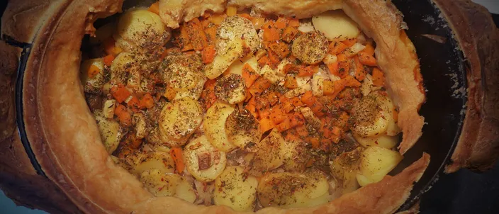 A baeckeoffe just opened in its dish: the baked dough seal torn back around the rim over layered potato slices, carrot and herbs