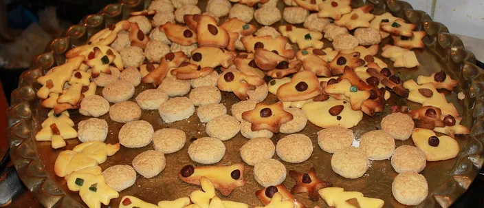 A brass tray of homemade Alsatian Christmas cookies: butter stars and bells, round almond cookies and shapes topped with candied fruit