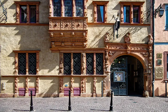 The Renaissance facade of the Maison des Têtes in Colmar, its oriel window and doorway framed in carved stone heads and masks