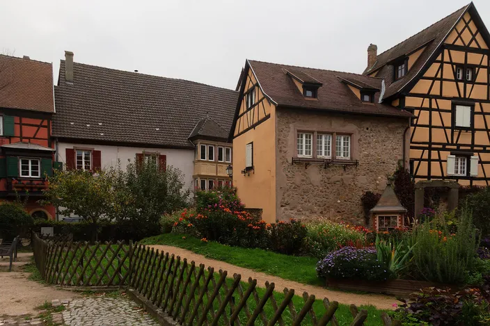 Half-timbered and stone houses behind a garden and a wooden fence in Turckheim, Alsace