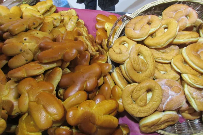 A market table piled with manala, the small brioche men of Saint Nicholas, beside a basket of sugared pretzels