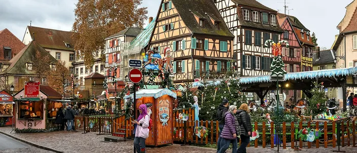 Half-timbered houses around a cobbled square in Colmar's Little Venice, the children's Christmas market below them with its fenced nativity, small wooden huts and decorated trees