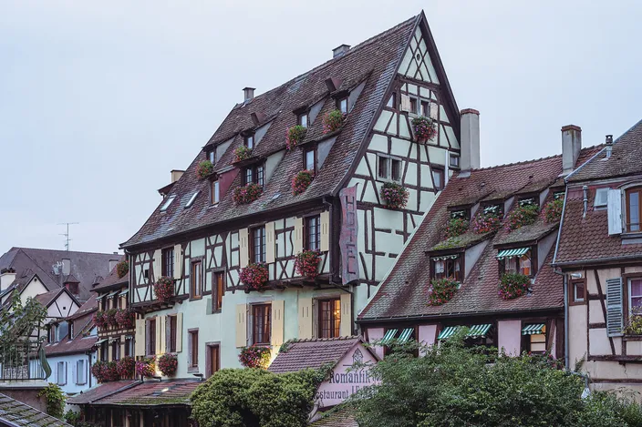 Tall half-timbered houses with red geraniums at their windows above the water in Petite Venise, Colmar, in the blue hour