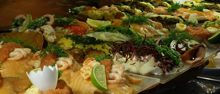 A glass counter of composed smørrebrød: pieces of rye heaped with smoked salmon, shrimp, egg, roe, dill and lemon, laid out in rows